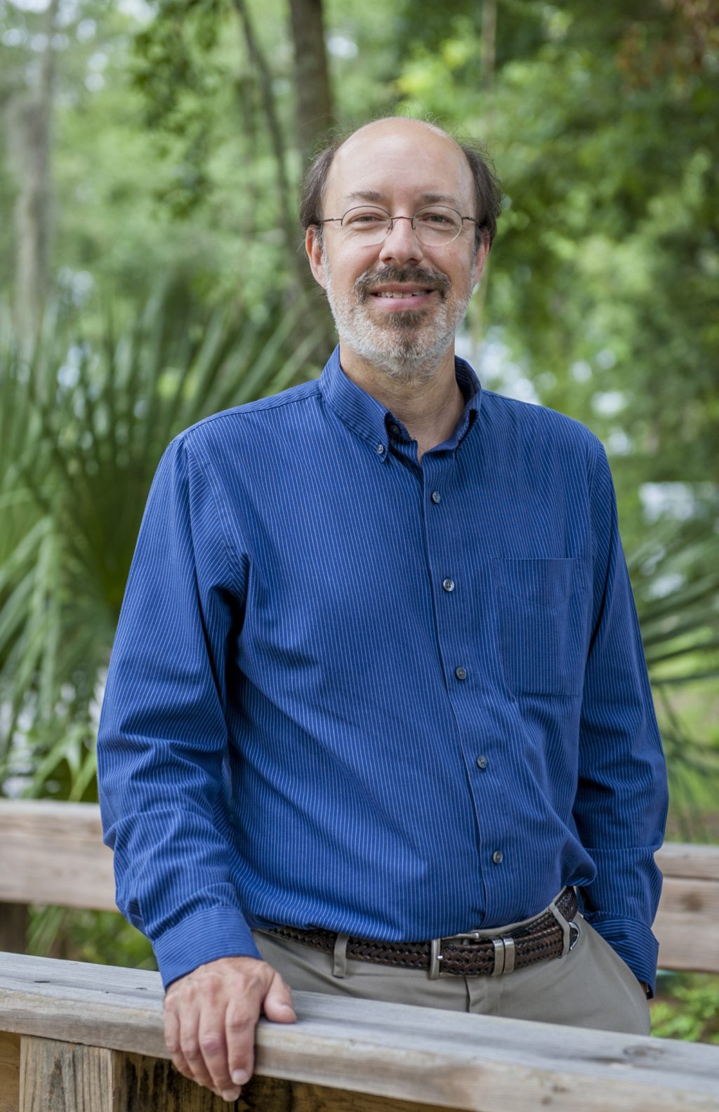 Person smiling for camera on a wooden walk bridge in a forest.