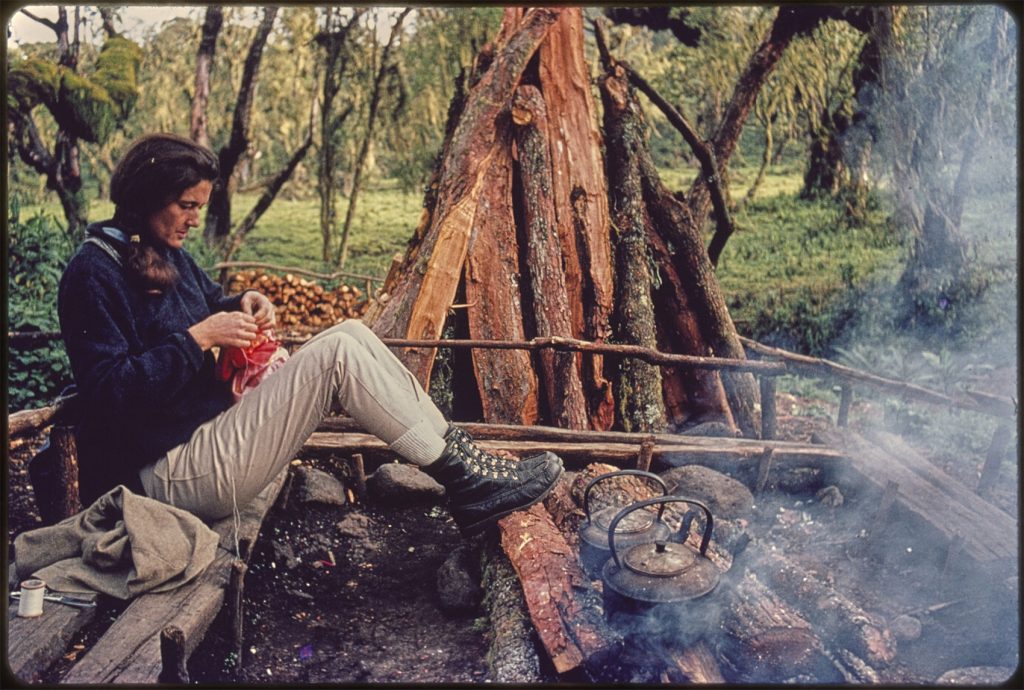 woman sits on low wooden bench in front of a fire